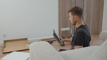 Man assembles cabinet drawers using tools on living room floor. Concept of DIY home improvement and furniture installation video