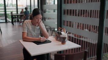 Serene Reflection in Cafe A young individual is engrossed in creative pursuits, seated alone, with an open window nearby. The scene is infused with a peaceful ambiance. video