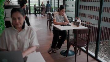 Cafe Ambiance capturing the charm of cafe setting, Two ladies are engrossed in their respective activities within a trendy and stylish cafe. The warm lighting, comfortable seating. video