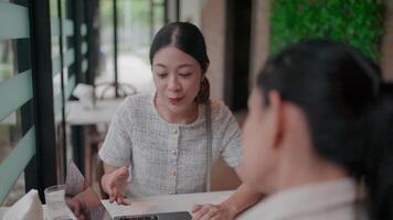 Business Collaboration Two businesswomen having a goal oriented conversation sitting at an indoor table with open notebooks and laptops for use in their work environment. video