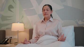 A woman finds serenity amidst the comfort of her bed, practicing mindfulness with her eyes closed and hands in a meditative gesture. video