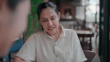 A woman in a light-colored shirt engaged in a pleasant conversation with an individual, their faces illuminated in the warm glow of a restaurant setting. video
