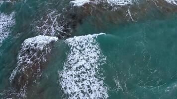 Aerial view of turquoise ocean waves with dynamic white foam patterns and depth variations creating a serene and visually rich seascape under sunlight video