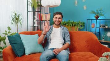 Indian man smiling friendly at camera, waving hands gesturing hello, hi, greeting at home on sofa video