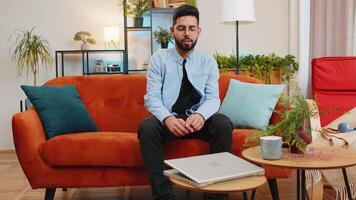 Happy young Indian man typing working on laptop browsing internet using apps sitting on home sofa video