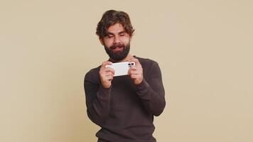 Addicted man enthusiastically playing racing games on mobile phone against beige background video