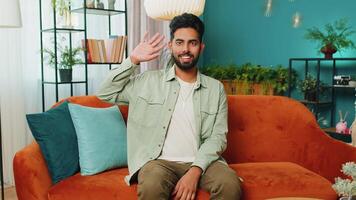 Indian man smiling friendly at camera, waving hands gesturing hello, hi, greeting at home on sofa video