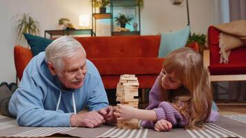 Excited little cute girl granddaughter playing building block game with smiling grandfather at home video