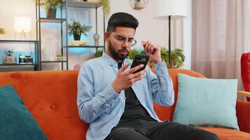 Shocked sad Indian young man using smartphone reading negative message feels annoyed app crash video