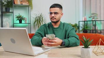 Smiling happy man counting money cash and use laptop pc calculate domestic income earnings at home video