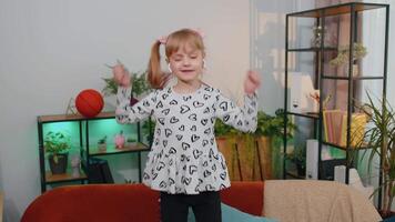 Happy child girl kid wears earphones dancing and jumping while listening to the music at home alone video