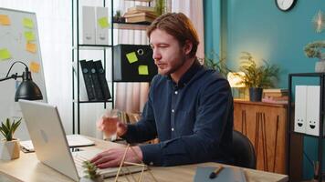 Businessman sitting at workplace desk drinking water while working with laptop in home office video