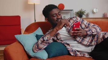 Cheerful young man lying on sofa, using mobile phone share messages on social media application video