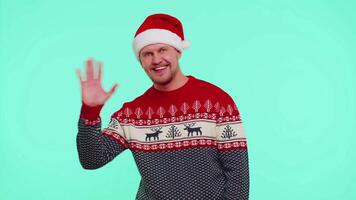 Man in red Christmas sweater waves hand palm in hello gesture welcomes someone to celebrate New Year video