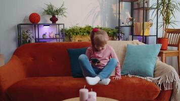 Child toddler hold smartphone watching funny cartoons, chatting with friends on couch alone at home video