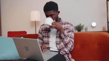 Young man using laptop computer lying on sofa at home working, online shopping from home office video