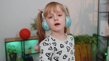 Happy child girl kid in headphones dancing and jumping while listening to the music at home alone video