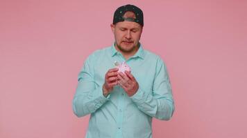 Poor man upset over insufficient amount of money, holding piggybank, one dollar banknote, bankruptcy video