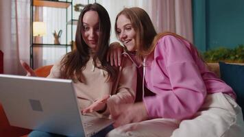 Young adult women couple looking at laptop notebook screen making online shopping purchase at home video
