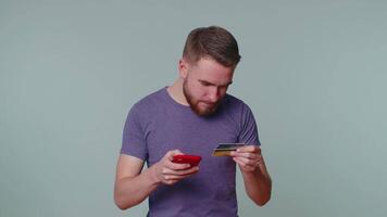 homem usar Móvel célula telefone e plástico crédito banco cartão, navegando dizer Uau sim encontrado Fora ótimo grande ganhar video