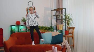 Happy child girl kid in headphones dancing and jumping while listening to the music at home alone video