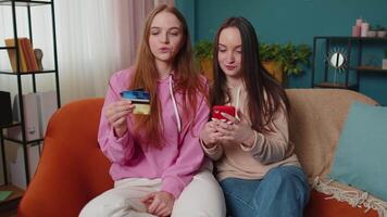 Cheerful girls friends using credit bank card and smartphone while transferring money, purchases video