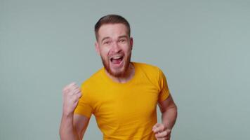 Stylish man in t-shirt shouting, raising fists in gesture I did it, celebrating success, winning video