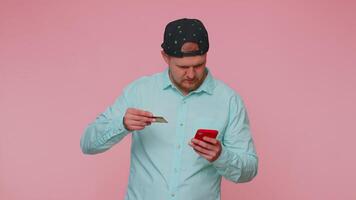 Man use mobile cell phone and plastic credit bank card, browsing say wow yes found out great big win video