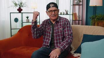 Grandfather man shouting, raising fists in gesture I did it, celebrating success, winning at home video