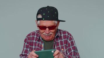 Worried funny addicted senior man enthusiastically playing drive racing games on mobile phone video