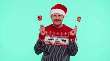 Funny man in red New Year sweater holding candy striped lollipops hiding behind them, fooling around video