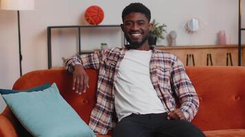Young man smiling friendly at camera, waving hands gesturing hello, hi, greeting at home on sofa video