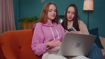 Happy girls friends using credit bank card and laptop while transferring money, purchases at home video