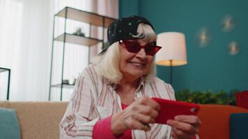 Worried funny grandmother woman enthusiastically playing racing games on mobile phone at home video