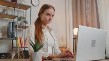 Young woman girl using laptop computer sitting at table working, typing on keyboard from home office video