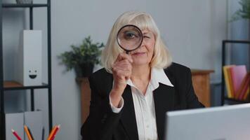Senior business woman looks through a magnifying glass, investigate, examine, analyzing, reading video