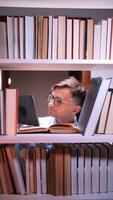 vertical universidade aluna vestindo óculos lendo uma tábua e livros entre prateleiras dentro uma biblioteca às noite, cercado de livros e usando uma tábua video