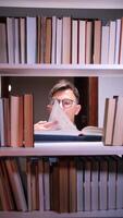 vertical Young college student wearing eyeglasses reading a book between bookshelves in a library, enjoying the quiet atmosphere and expanding his knowledge video