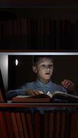 vertical Curious boy reading a glowing magic book among other books in a library at night, captivated by its bright light, experiencing wonder and imagination in a world of stories video