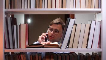 A man in glasses is talking on a phone while looking at books video