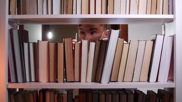 Librarian with eyeglasses looking for book between bookshelves, searching for information in library or bookstore, surrounded by colorful books video
