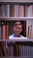 vertical Young male librarian having a good idea while standing between bookshelves and pointing his index finger up, surrounded by books in a library or bookstore video