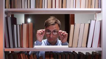 Exhausted male student taking off glasses and rubbing his tired eyes, suffering from eye strain after long hours of reading and studying in the library surrounded by books video