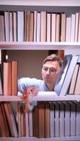 vertical Male librarian cleaning a white bookshelf with a rag, surrounded by books in a library or bookstore, ensuring a tidy and organized environment for readers video