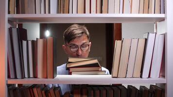 Young college student searching for interesting literature in a library at night, holding a stack of books while navigating the dimly lit shelves filled with knowledge video