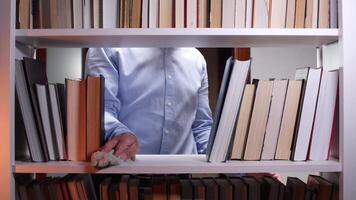 Male librarian cleaning a white bookshelf with a rag, surrounded by books in a library or bookstore, ensuring a tidy and organized environment for readers video