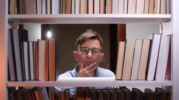 Young male librarian having a good idea while standing between bookshelves and pointing his index finger up, surrounded by books in a library or bookstore video