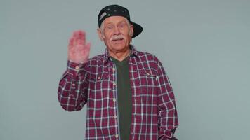 Senior man smiling friendly at camera and waving hands gesturing hello or goodbye, welcoming video
