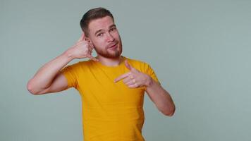 Cheerful one man in t-shirt looking at camera doing phone gesture like says hey you call me back video
