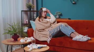 Portrait of young woman suffering from cold or allergy in plaid lying on sofa in living room at home video